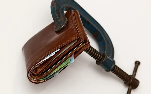 Wallet squeezed in a clamp symbolizing debt