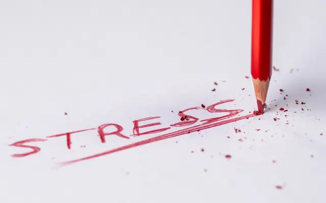Red pencil erasing the word stress on paper