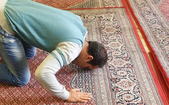Man prostrating in prayer on a prayer rug